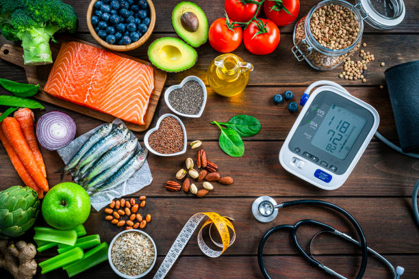 Healthy food for heart care: overhead view of healthy food rich in Omega-3 and antioxidants and a blood pressure monitor, tape measure and stethoscope shot on wooden table. The composition includes a salmon fillet, sardines, avocado, extra virgin olive oil, brown lentils, celery, artichoke blueberries, celery, carrots, brown lentils, asparagus, artichoke, broccoli, flax seeds, chia seeds and some nuts like almonds, pistachio and pecan. High resolution 42Mp studio digital capture taken with SONY A7rII and Zeiss Batis 40mm F2.0 CF lens