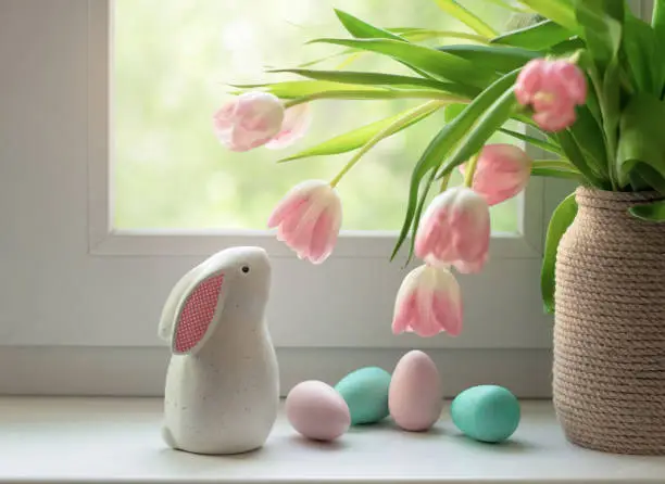 Photo of Ceramic Easter bunny, colorful dyed eggs and tulip flowers on windowsill. Decorations for Easter celebration at home