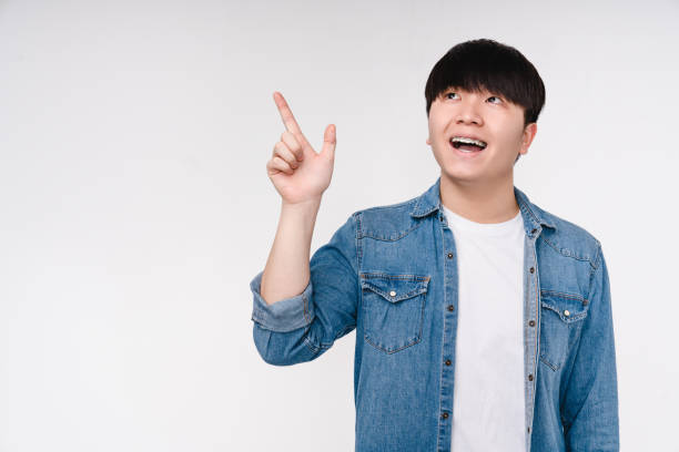 istock Impressed happy young korean asian man boy showing pointing at copyspace free space for advertise looking upwards isolated on white background 1371125918