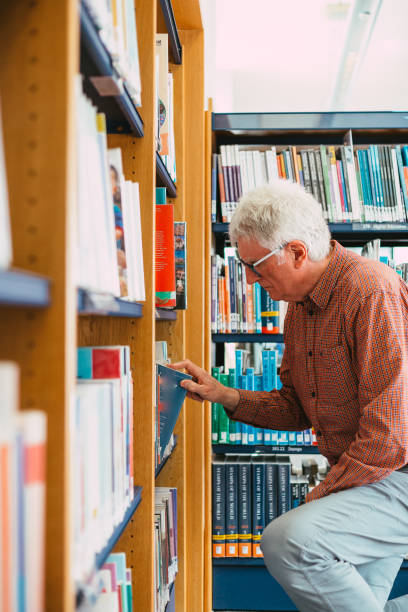 istock Senior man looking at books on shelf in library 1371126112