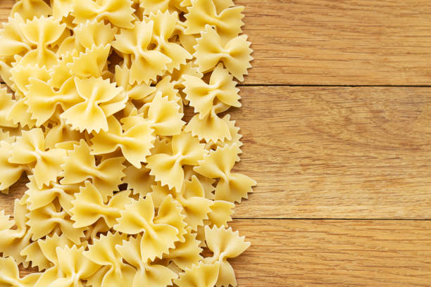 sterta surowego włoskiego makaronu farfalle na drewnianym stole - bow tie pasta italian cuisine bow heap zdjęcia i obrazy z banku zdjęć