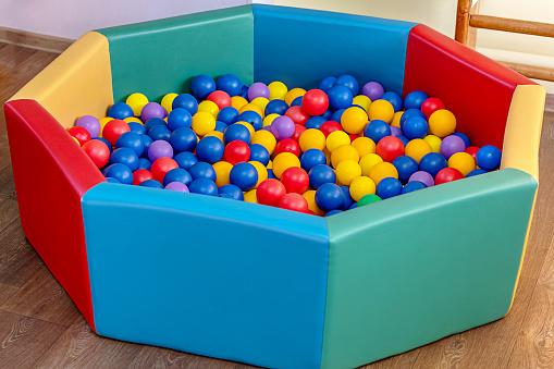 Small pool with colorful plastic balls stands on wooden floor of children room for game and entertainment.