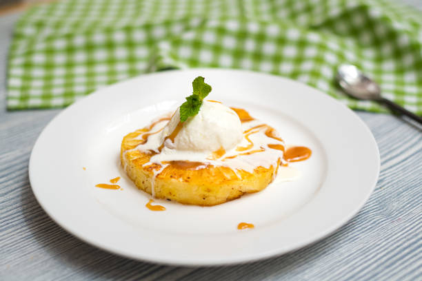 A ball of creamy vanilla ice cream on a slice of fried pineapple with caramel sauce. One serving on a white plate. stock photo