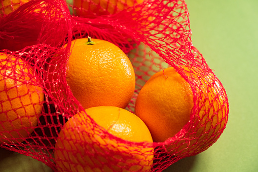 Fresh oranges from supermarket in plastic mesh  on green background.