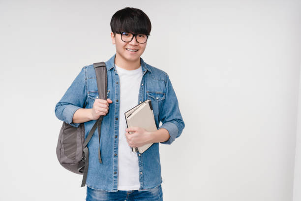 lächelnd mit zahnspangen junger asiatischer koreanischer smart man student high schoolboy hält lehrbücher und notizbücher, trägt eine tasche, geht zur universität schule college isoliert in weißem hintergrund - southeast asia fotos stock-fotos und bilder