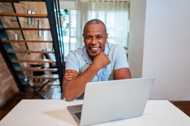 istock Mature man using laptop at home - looking at camera 1371131904