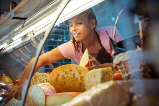 Saleswoman arranging cheese in display cabinet Saleswoman arranging fresh cheese in display cabinet. Female owner is working at convenience store. She is at delicatessen. display cabinet stock pictures, royalty-free photos & images