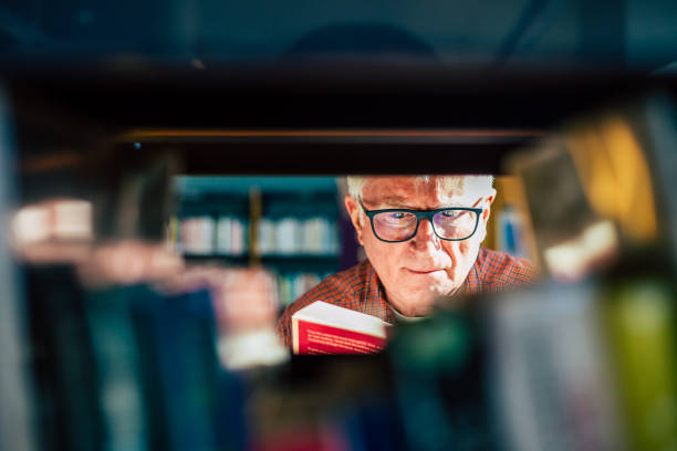 hombre mayor mirando libros en el estante de la biblioteca - professor librarian university library fotografías e imágenes de stock