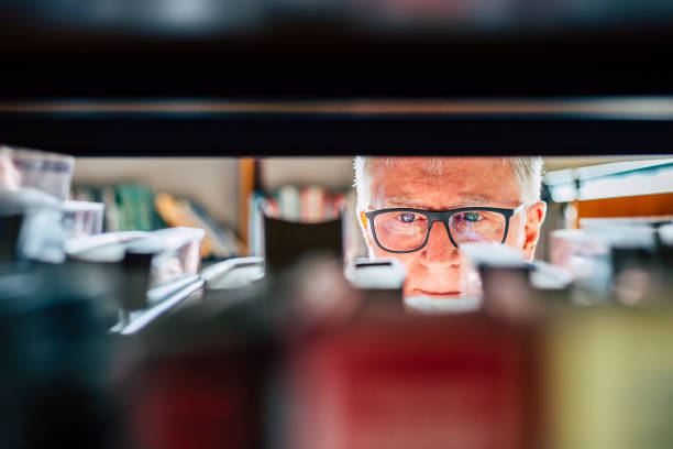 Senior man looking at books on shelf in library