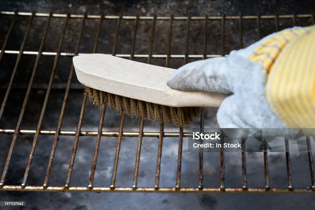 Wooden wire brush cleans dirty barbecue grill rust. Leather protection gloves. Barbecue Grill Stock Photo
