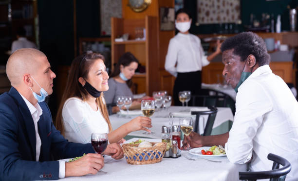 Cheerful people in masks having dinner in restaurant
