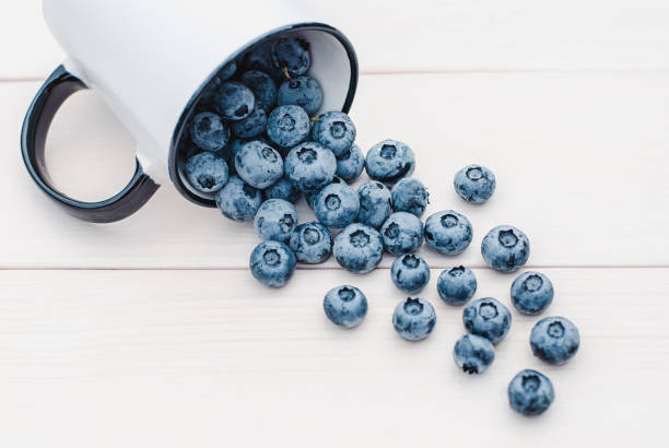 Blueberries slop out of a mug on white wooden table, blueberry fruit in a cup Blueberries slop out of a mug on white wooden table, blueberry fruit in a cup Cup of Blueberries stock pictures, royalty-free photos & images