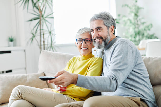 älteres paar, das zusammen glückliches reifes fernsehen fernsieht - senior women electronics people remote control stock-fotos und bilder
