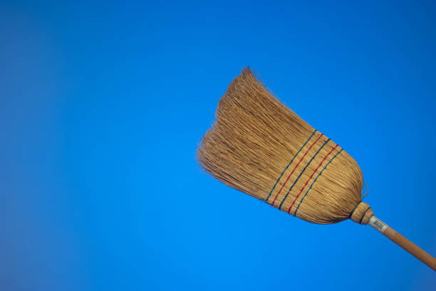 Straw broom with wooden handle. Close up studio shot, isolated on blue background.