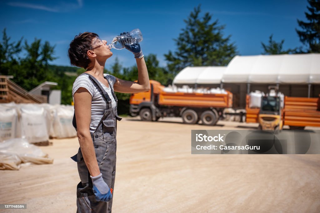 Thirsty Female Blue-collar Worker in Ore Processing Plant Thirsty Female Blue-collar Worker in Ore Processing Plant. Heat - Temperature Stock Photo