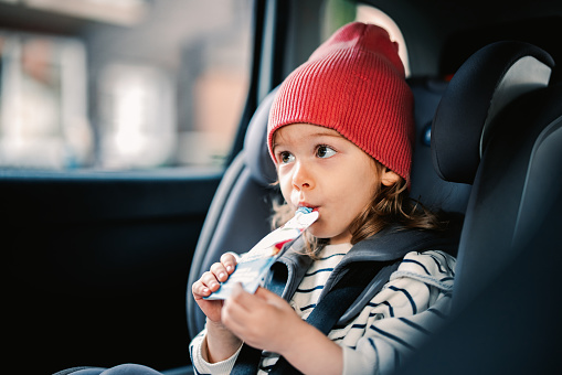 Happy girl enjoying juice while sitting in car safety seat.