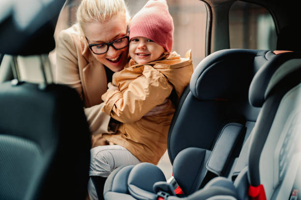 portrait of happy mother putting her little daughter in a car safety seat - blond hair carrying little girls small imagens e fotografias de stock