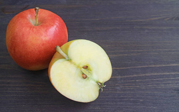 frisch reifer halb geschnittener roter apfel mit einer ganzen frucht auf schwarzem holztisch - gezweitelt stock-fotos und bilder