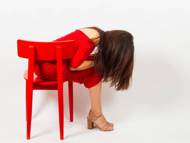 An Asian woman with long hair in a red dress sits on a red chair and looks down, covering her face with her hair.