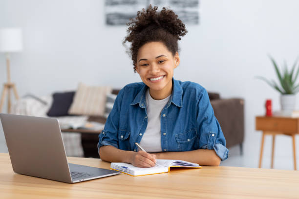 istock Distance learning, online education. Portrait of smiling young female freelancer working in co-working, modern office or home. African American woman using laptop computer looking at camera, smiling 1371153473