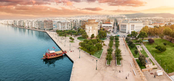 Aerial panoramic view of the main symbol of Thessaloniki city - the White Tower with boat tour ship at the pier. Concept of travel landmarks in Greece and urban development. stock photo