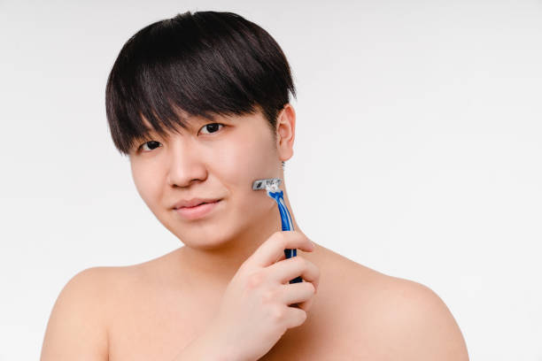attraktiver junger asiatischer koreanischer hemdloser nackter mann, der sich mit rasiermesser rasiert und in die kamera schaut. morgendliches hygienekonzept. männliche schönheit - shower portrait male beauty chest stock-fotos und bilder