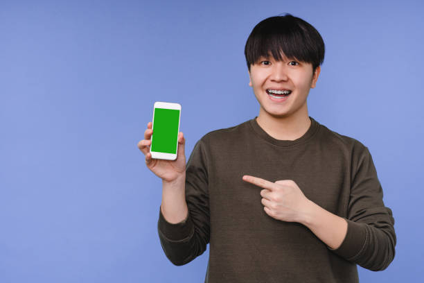 istock Young korean asian man boy freelancer student pointing at smart phone cellphone blank screen with mockup copy space, showing advert, using online application isolated in blue background 1371157178