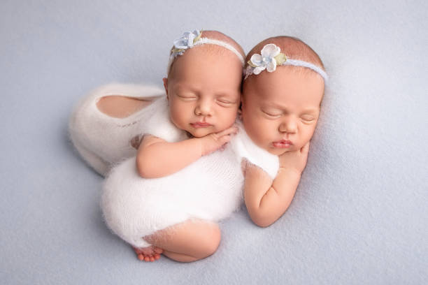 piccole gemelle appena nate. un gemello appena nato abbraccia e dorme su sua sorella, le gemelle appena nate contro una coperta blu pallido con bende bianche e delicati body di lana bianca. - twin newborn baby baby girls foto e immagini stock