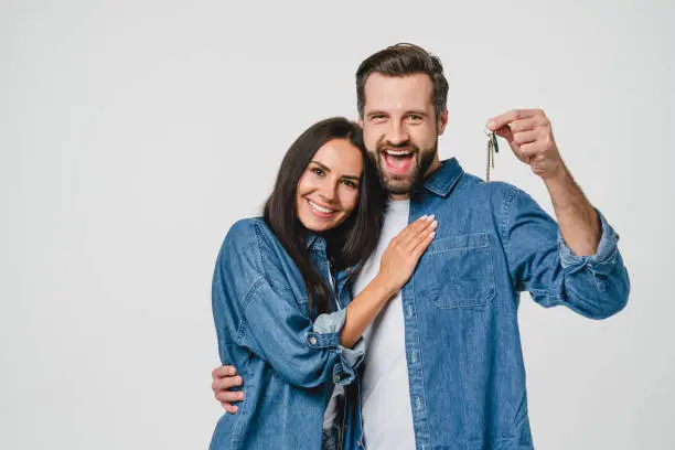 Photo of Homeowners. Happy young caucasian couple spouses wife and husband holding car house flat appartment keys, celebrating new purchase buying real estate isolated in white background. Mortgage loan