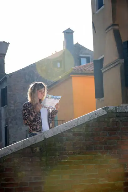 Photo of Young blonde woman reading a newspaper or magazine near the historical building of the old city