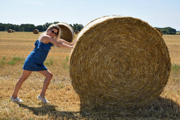 istock Young woman smiling jokingly pushes a round haystack in a cereal field 1371162767