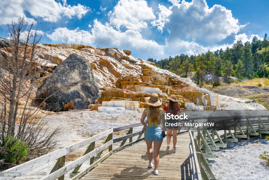 Women hiking on summer vacation in  Yellowstone National Park. Friends on sightseeing summer trip. Girls hiking on vacation next to Devils Thumb in Mammoth Hot Springs Lower Terrace, Yellowstone National Park, Wyoming, USA. Yellowstone National Park Stock Photo