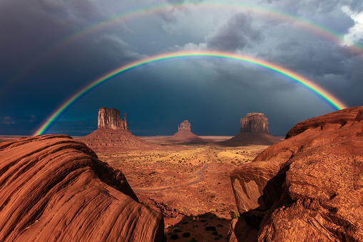 A vivid double rainbow over the iconic Mittens Buttes after a storm in Monument Valley Tribal Park, Arizona, USA.