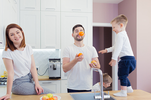 Young family in the kitchen preparing breakfast from fresh fruit, children help their parents, laugh, have fun