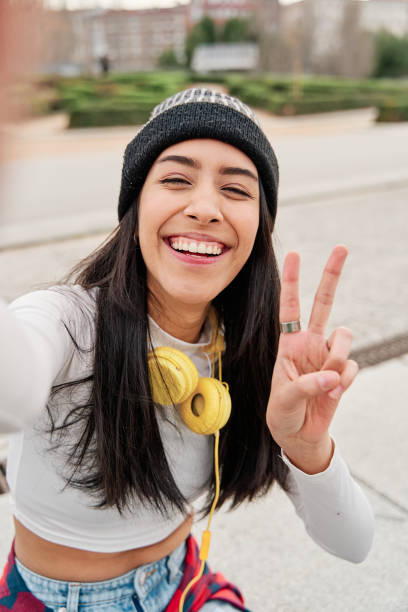 selfie einer jungen latina, die lächelt und mit ihren fingern das peace-zeichen macht. - selfie stock-fotos und bilder