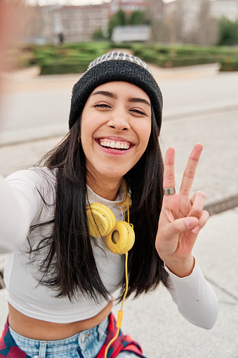 Selfie of a young latina while smiling and making the peace sign with her fingers.