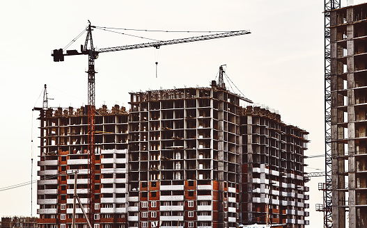 Construction site with frames of multistory buildings and cranes at white cloudy sky