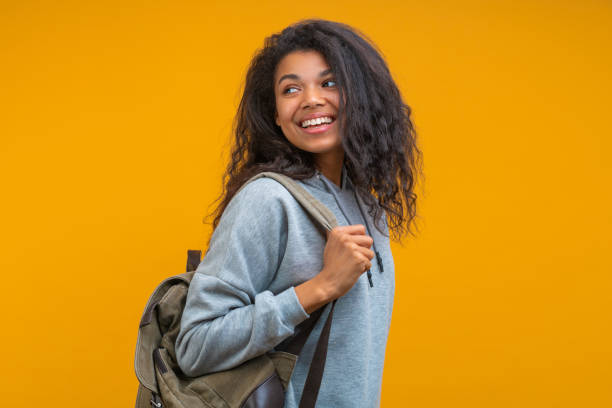 istock Beautiful smiling girl student posing with a backpack over bright colored orange yellow background and looking aside 1371177345