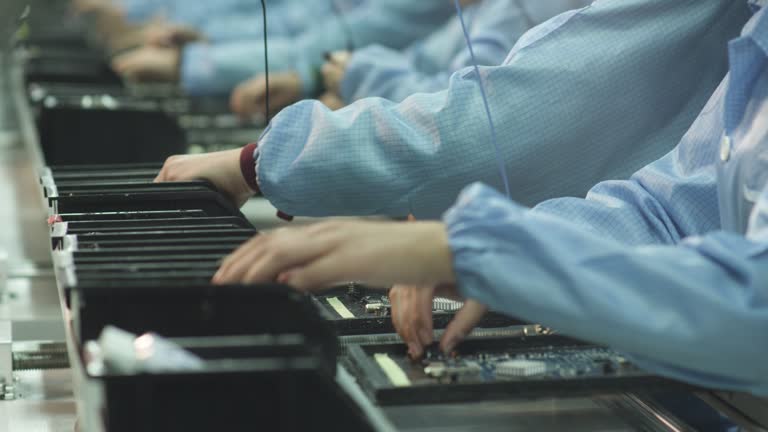 Workers install elements on an electronic circuit board at a TV factory