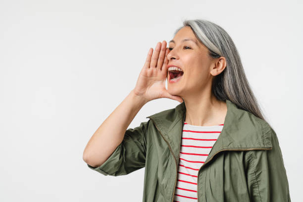 portrait recadré en gros plan d’une femme d’âge moyen mature de race blanche aux cheveux gris criant fort comme dans un haut-parleur à propos de l’offre de réduction isolée sur fond blanc - crier photos et images de collection