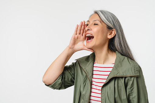Closeup cropped portrait of caucasian mature middle-aged woman with grey hair shouting loud like in loudspeaker about sale discount offer isolated in white background