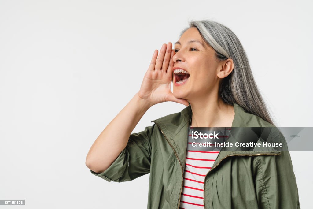 Closeup cropped portrait of caucasian mature middle-aged woman with grey hair shouting loud like in loudspeaker about sale discount offer isolated in white background Shouting Stock Photo