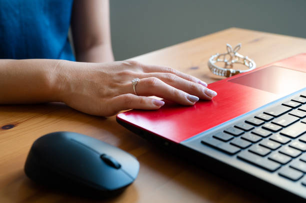 Close-up of woman hand with luxury accessories such as diamond ring while working on laptop at wooden desk.