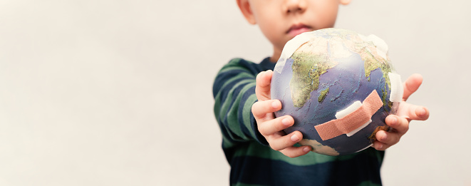 Banner of young little child boy holding and handing over a damaged globe with bandage. Environmental damage for global warming and climate change impact to next generation concept. Earth day.