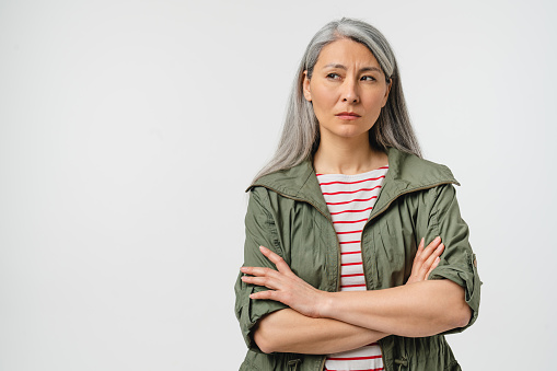 Thoughtful pensive contemplation of mature middle-aged caucasian woman with grey hair and casual clothes blowing her lips, feeling offended isolated in white background