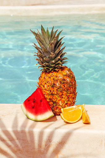 Summer fruits with watermelon, pineapple and orange by swimming pool in summer mood