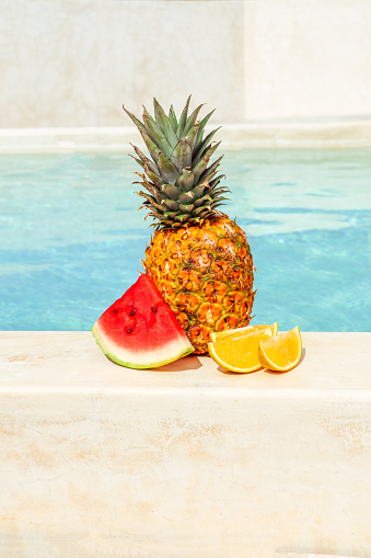 Summer fruits with watermelon, pineapple and orange by swimming pool in summer mood