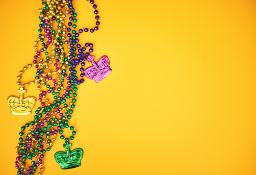 Mardi Gras background with colorful beads and crowns on a yellow background