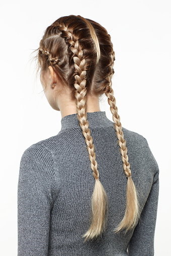 Back view portrait of beautiful young dark blonde woman. Female with creative braid hairdo on gray background.
