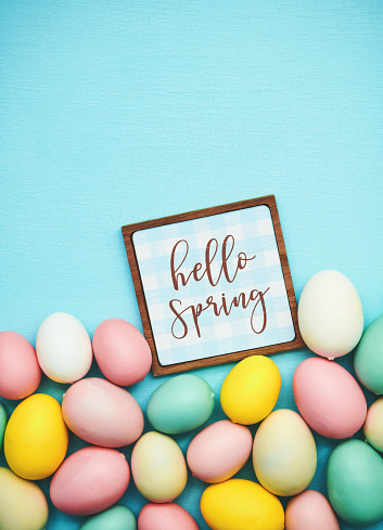 Hello Spring message on a blue background with collection of pastel colored Easter eggs